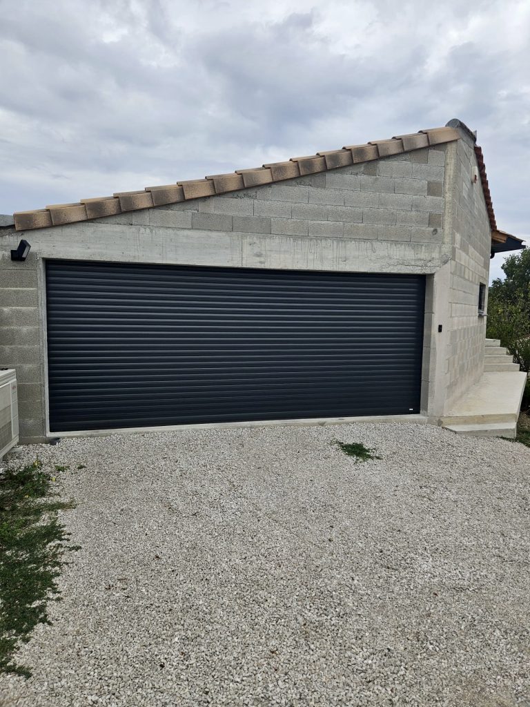 Garage moderne avec porte enroulable noire et façade en pierre