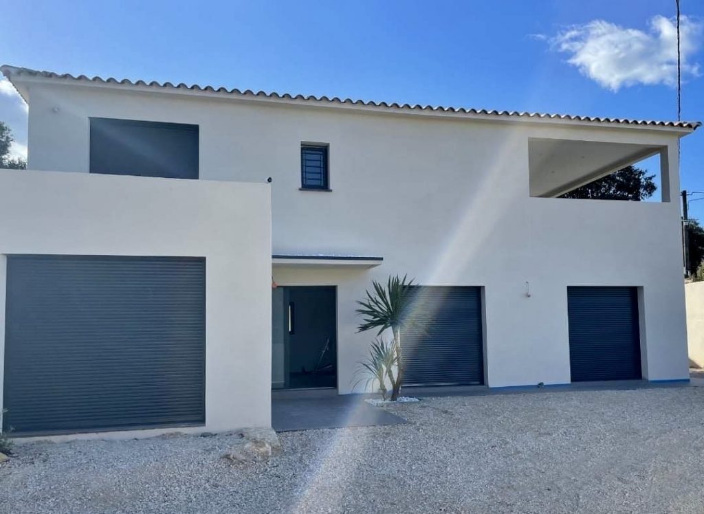 Maison moderne blanche avec portes garage bleues et terrasse couverte